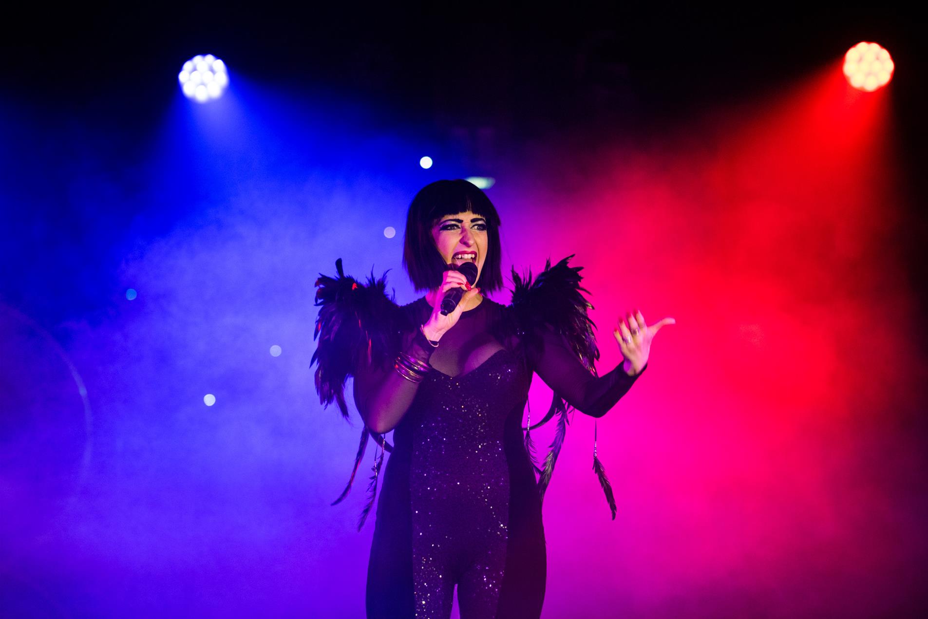 Performer in a black body suit singing on stage.