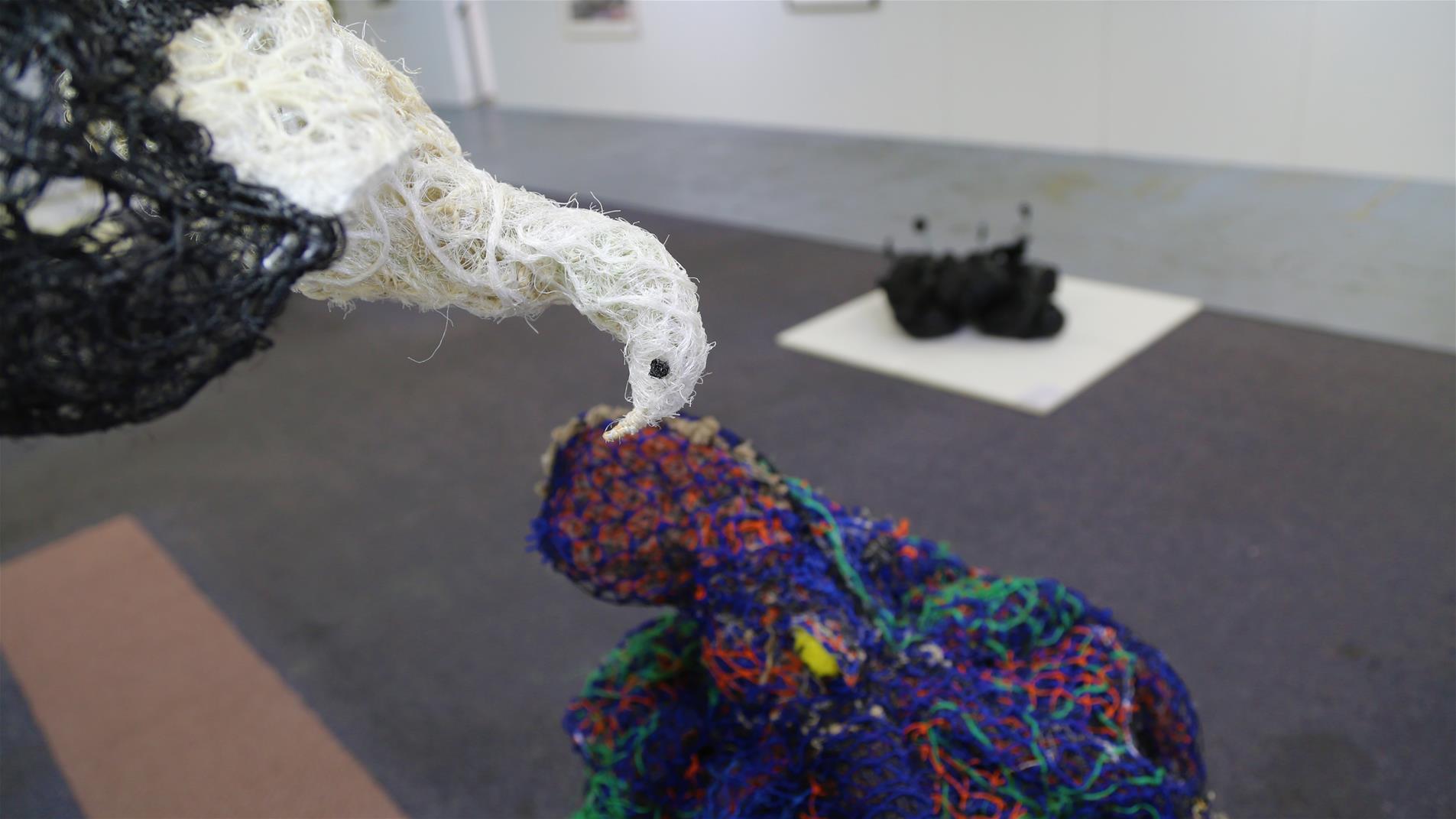 Colourful yarn sculpture and a bird made of yarn hanging in a gallery.