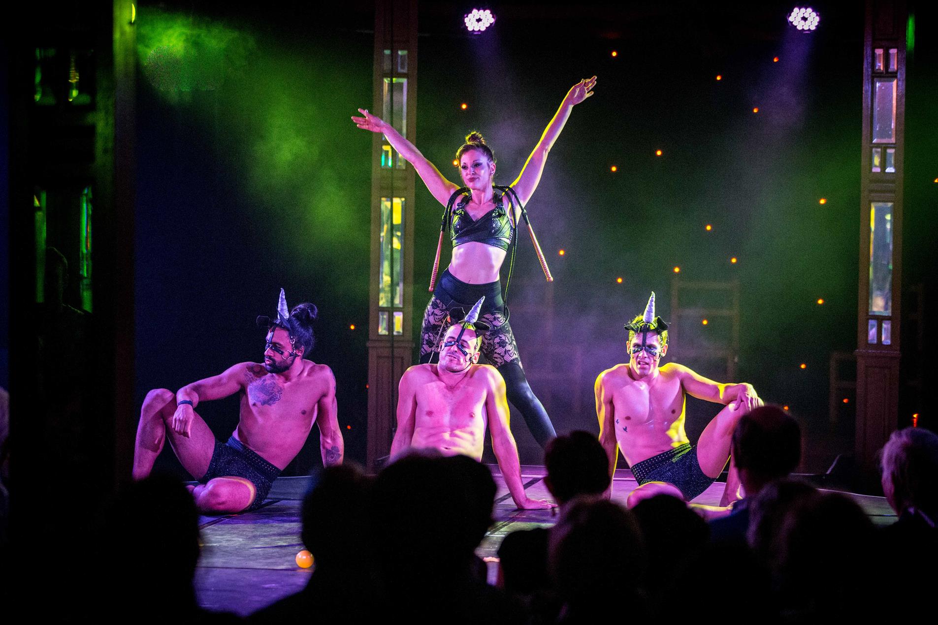 Female dancer in black outfit performing with three male dancers on stage.