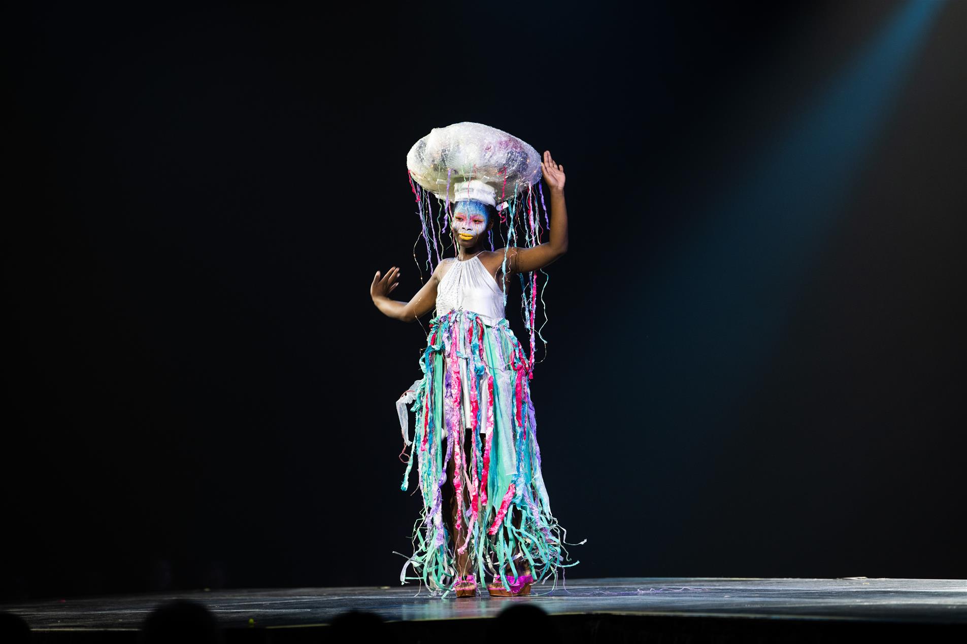 A model wearing colourful face paint and a vibrant dress on stage.