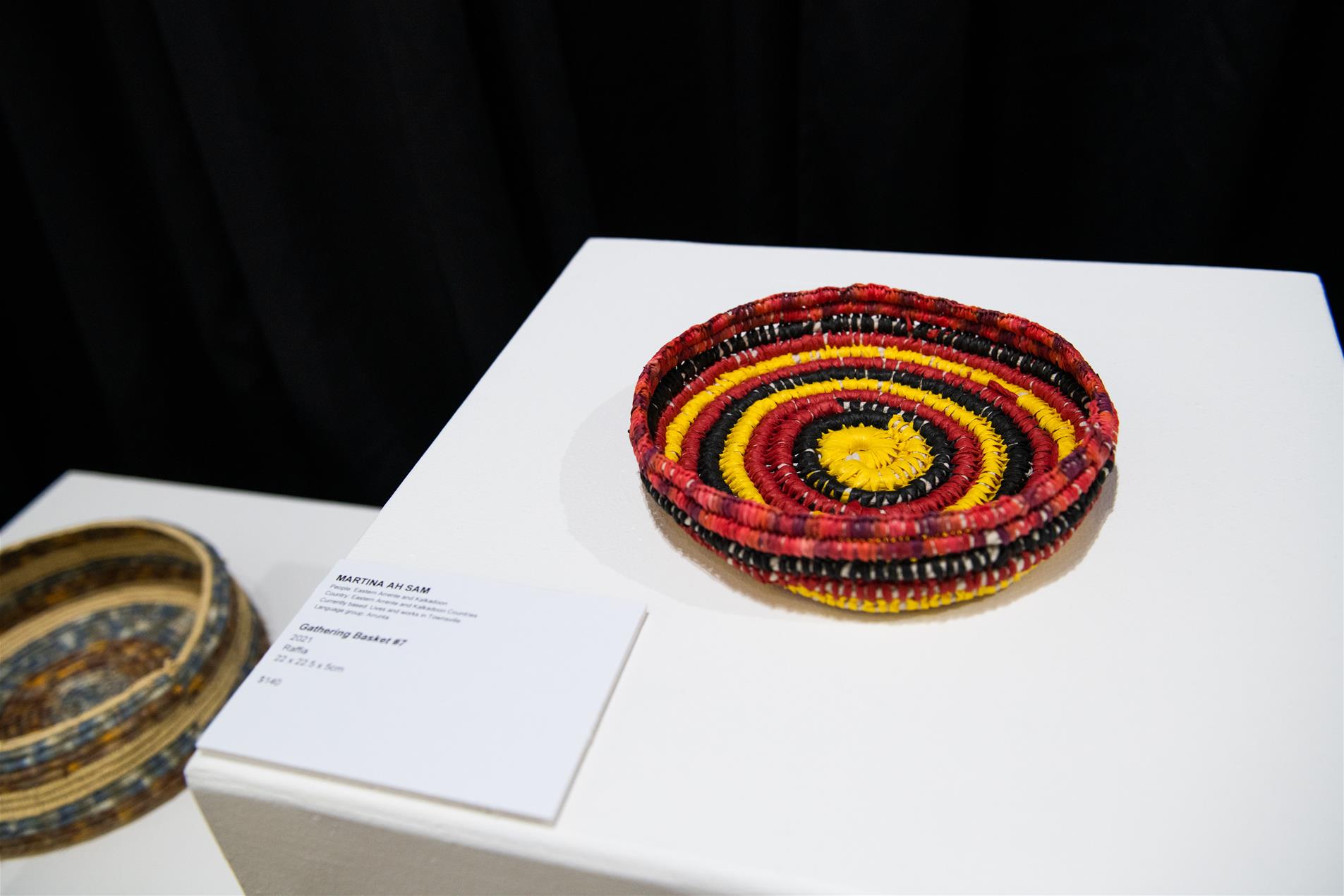 A red, black and yellow gathering basket displayed at an exhibition.