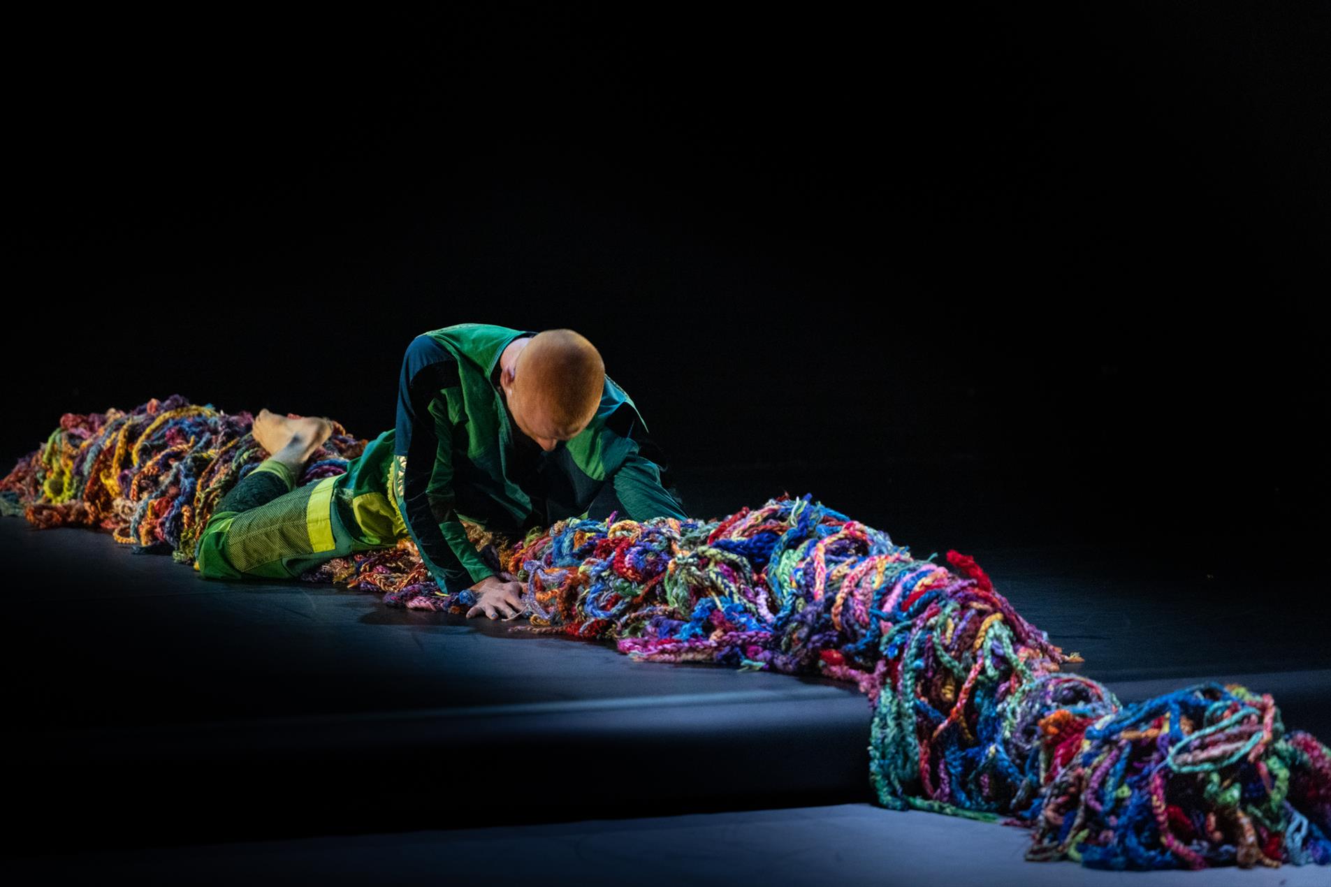 A male dancer laying on colourful wool performing on stage.