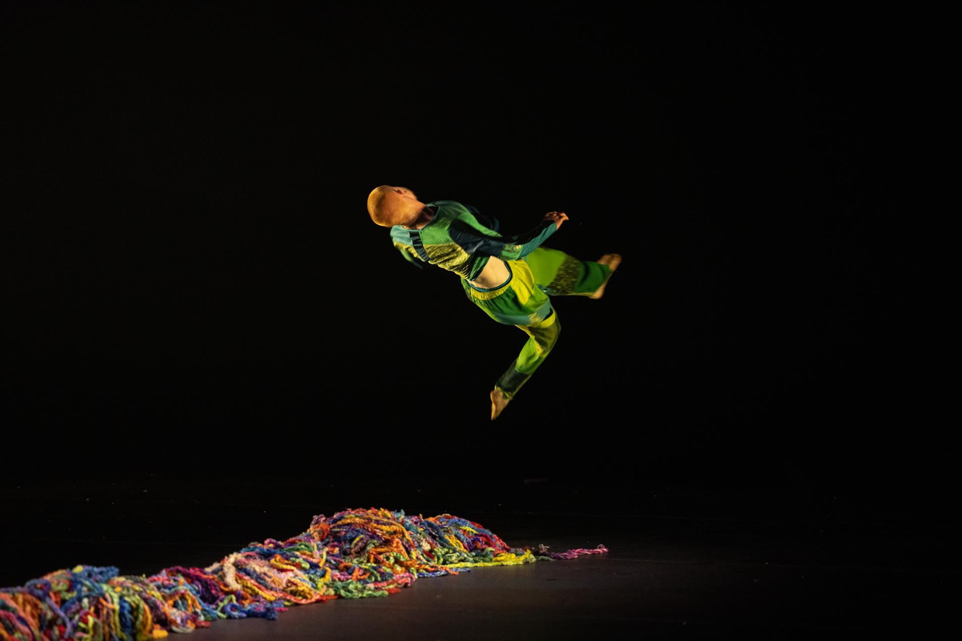 A male dancer performing on stage with colourful wool on the ground.