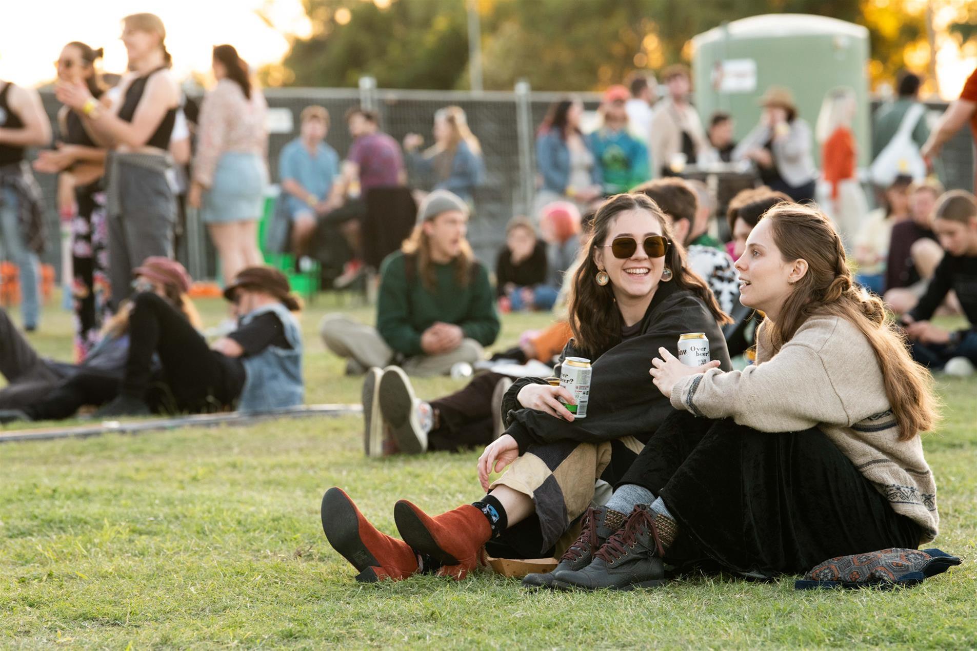 Two females sitting on the grass at a music festival.