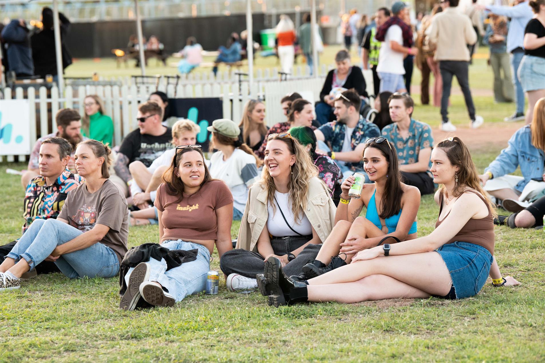 A group of people sitting on the grass at a music festival.