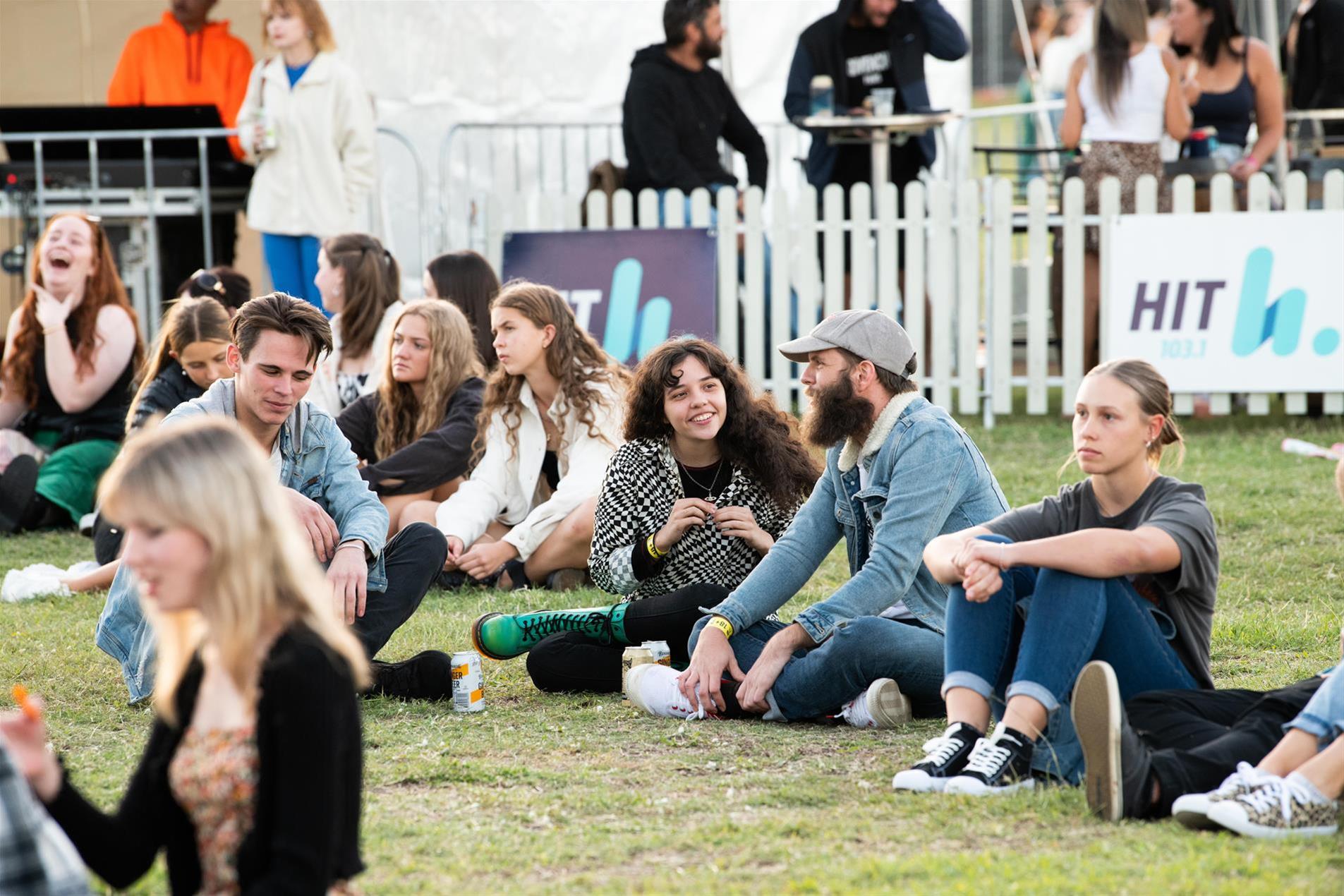 A group of people sitting on the grass at a music festival.