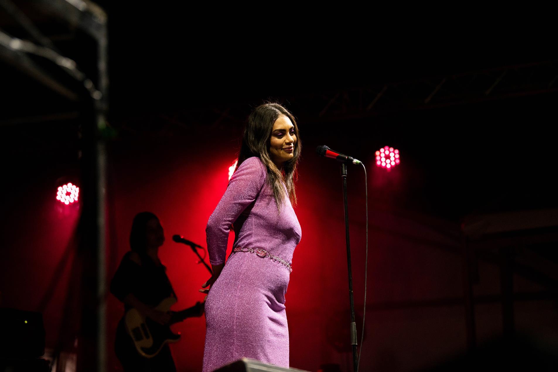 A solo female artist standing next to a microphone on stage.