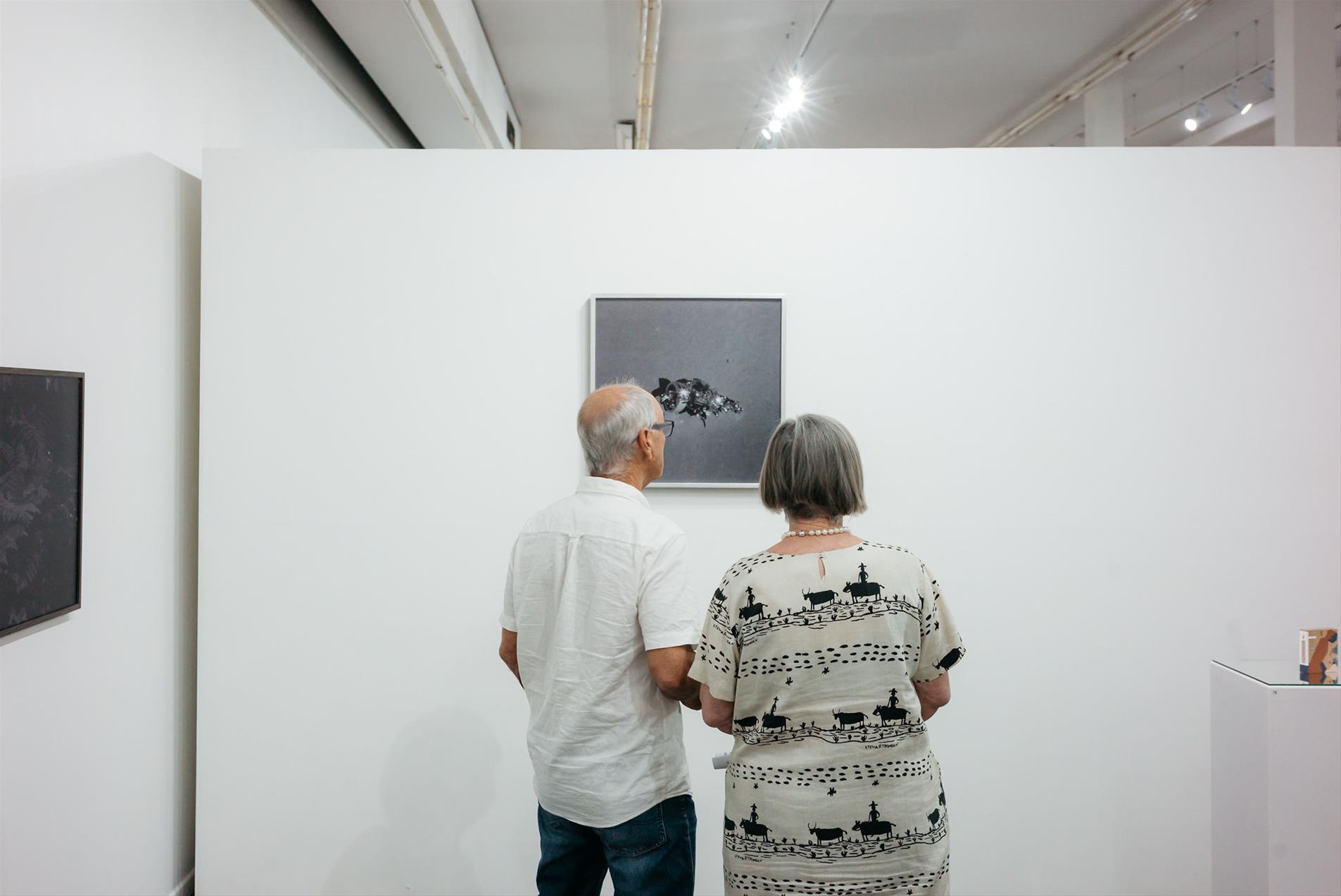 Two people standing in a gallery looking at a photograph on the wall.
