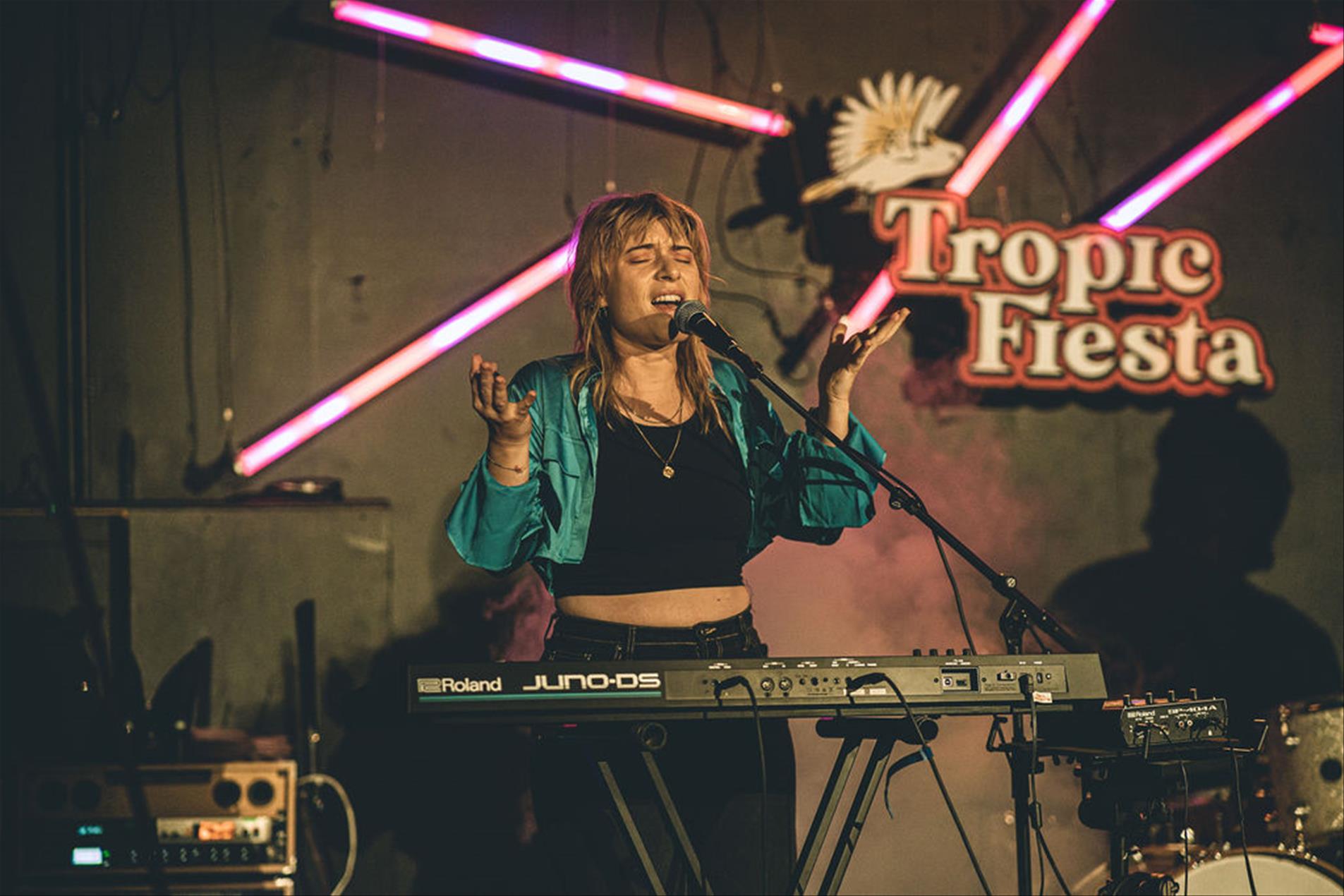 A female artist on stage with a microphone and a piano.