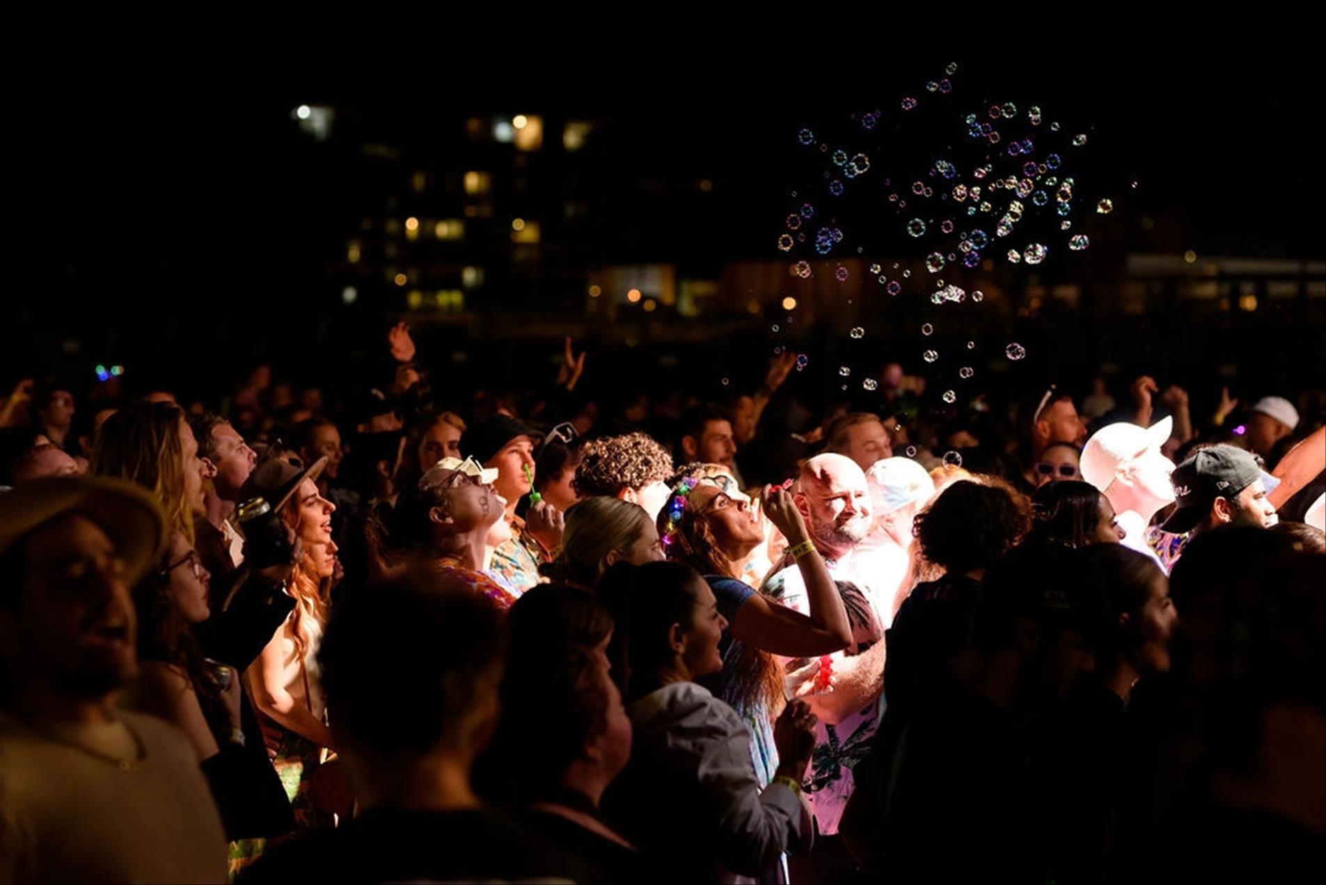 A crowd of people with a woman blowing bubbles into the air.