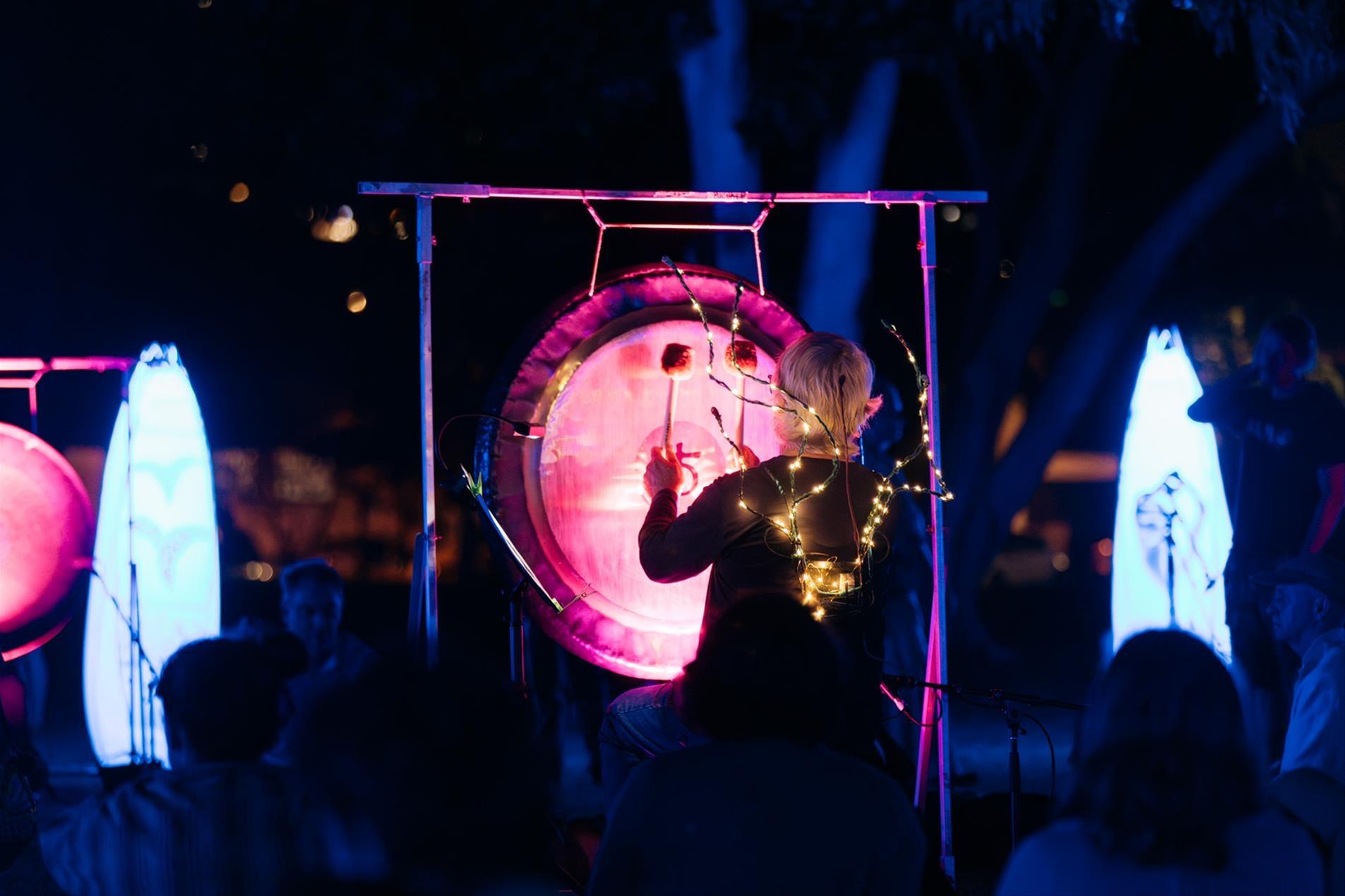 A man wearing a string of lights on his back while playing a drum.