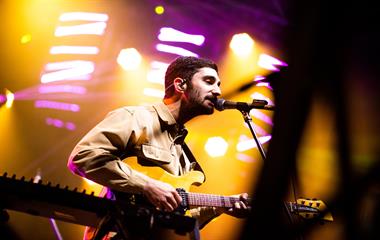 A male artist playing the guitar while singing into a microphone.