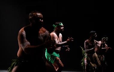 Four men in grass skirts with white body paint performing on stage.