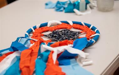 A dream catcher with blue and orange feathers hanging from it, placed on a table.