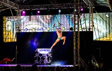 A male performer jumping out of a bowl of water into the air while holding ropes.