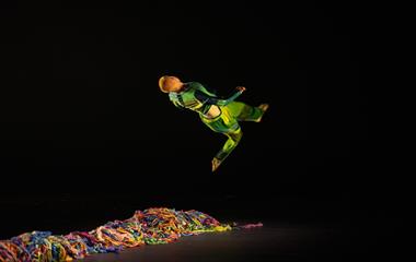 A male dancer performing on stage with colourful wool on the ground.