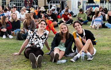 A group of people sitting on the grass at a music festival.