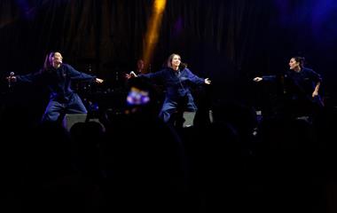 Three female artists performing on stage at a music festival.